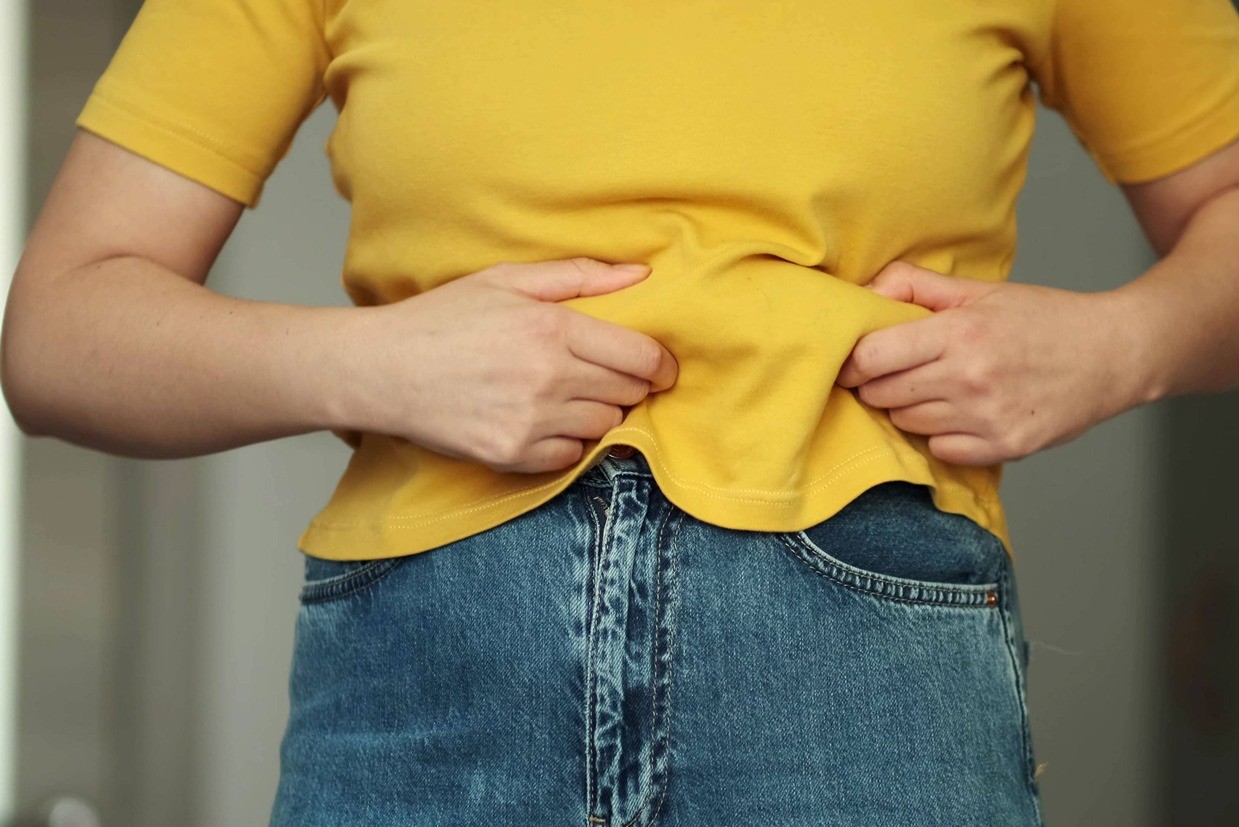 Woman wearing a yellow shirt holding her stomach.